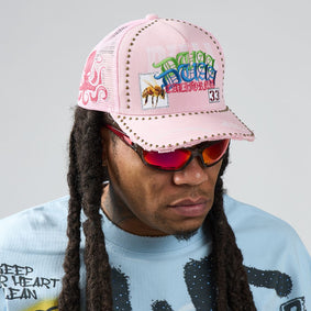 Person wearing a pink cap with colorful text and graphics, red sunglasses, and a light blue shirt with black text.