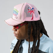 Person wearing a pink trucker hat with palm tree and flag designs on a gray background