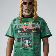 Man wearing a green graphic t-shirt with various designs and text on a plain background