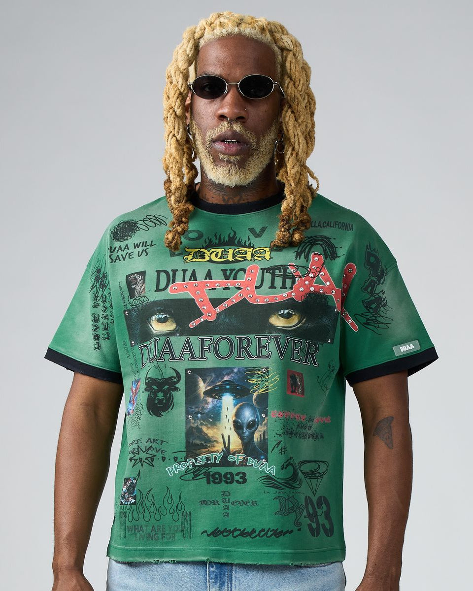 Man wearing a green graphic t-shirt with various designs and text on a plain background