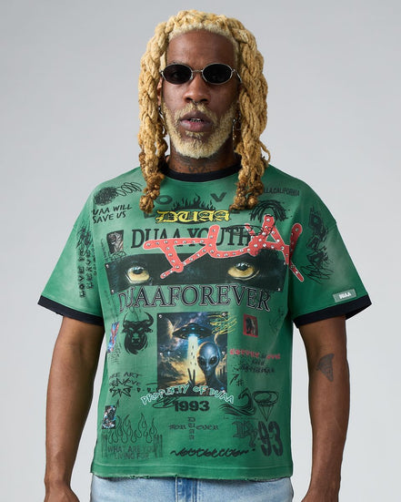 Man wearing a green graphic t-shirt with various designs and text on a plain background