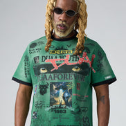 Person wearing a green graphic t-shirt with various designs and text on a plain background