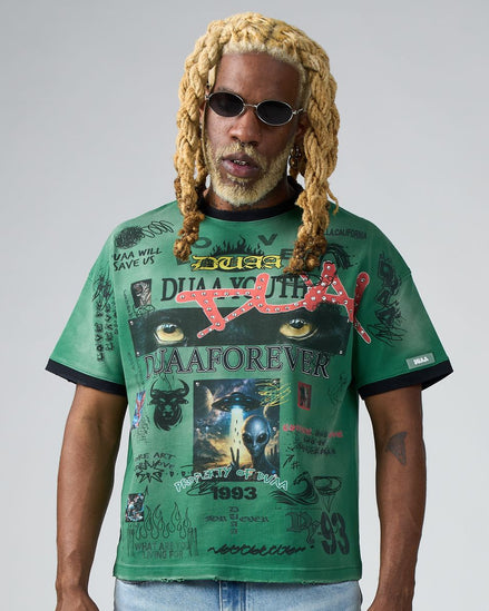 Person wearing a green graphic t-shirt with various designs and text on a plain background