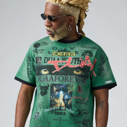 Man wearing a green graphic t-shirt with various designs and text on a plain background