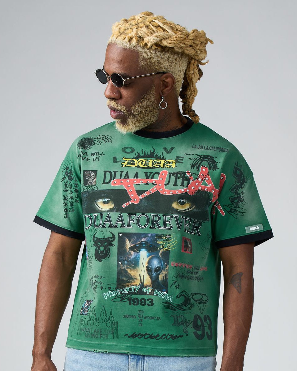 Man wearing a green graphic t-shirt with various designs and text on a plain background