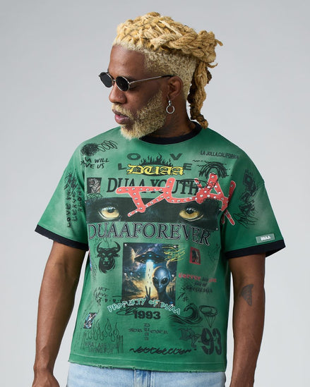 Man wearing a green graphic t-shirt with various designs and text on a plain background