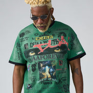 Man wearing a green graphic t-shirt with various designs and text on a plain background