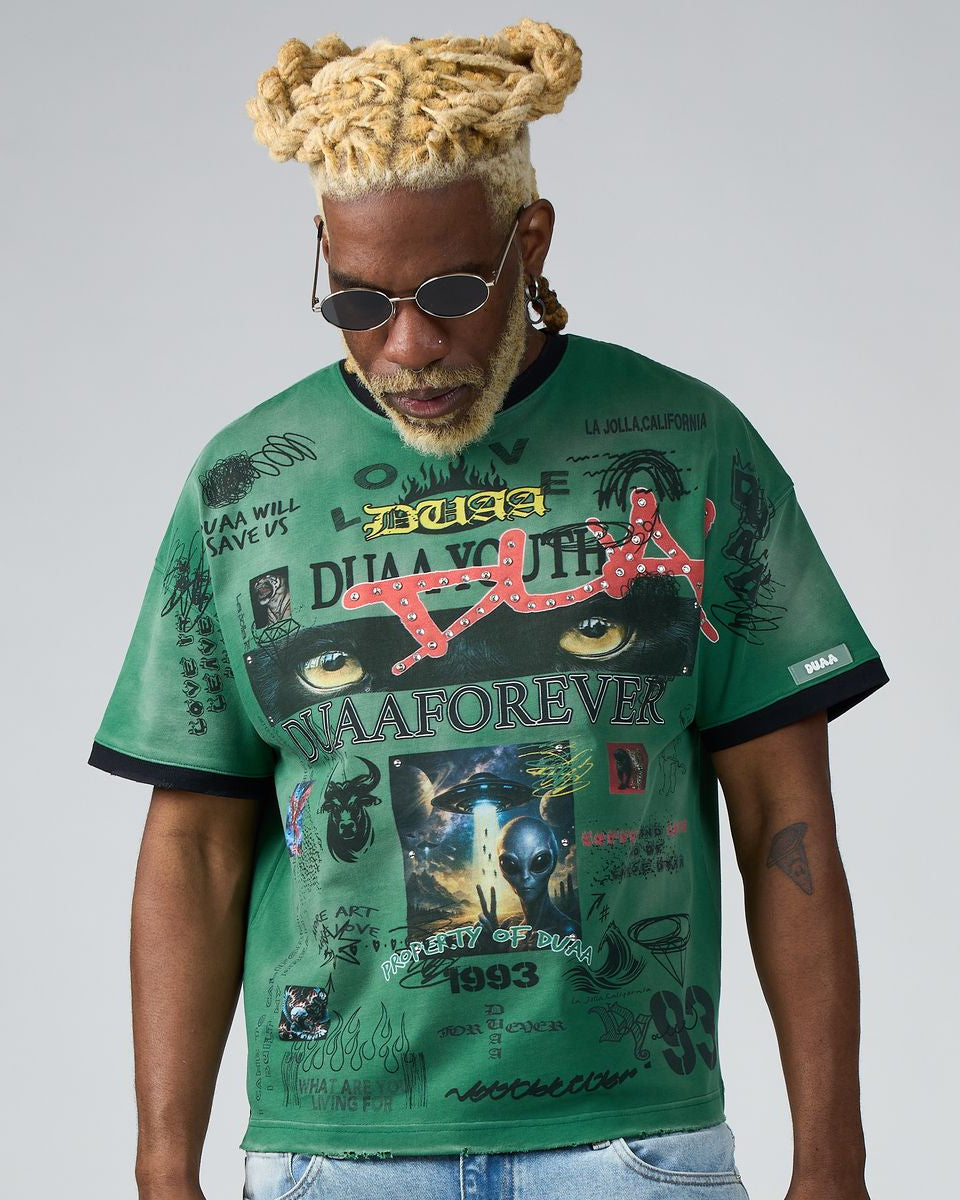 Man wearing a green graphic t-shirt with various designs and text on a plain background