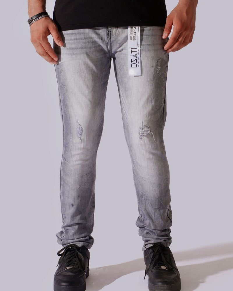 A person wearing light gray washed denim jeans with distressed details, paired with a black t-shirt and black sneakers, shown from the waist down against a light gray studio background.