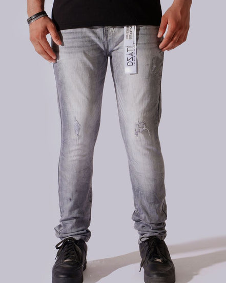 A person wearing light gray washed denim jeans with distressed details, paired with a black t-shirt and black sneakers, shown from the waist down against a light gray studio background.