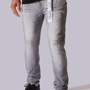 A person wearing light gray washed denim jeans with distressed details, paired with a black t-shirt and black sneakers, shown from the waist down against a solid gray background.