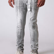 Person wearing light gray distressed jeans with a white label and white sneakers on a plain background