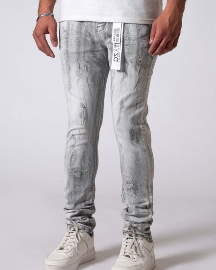 Person wearing light gray distressed jeans with a white label and white sneakers on a plain background