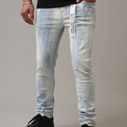Person wearing light blue distressed jeans with a brand label on a neutral background