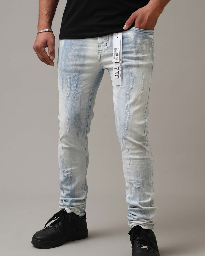 Person wearing light blue distressed jeans with a brand label on a neutral background