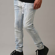 Person wearing light blue distressed jeans with a brand logo and black sneakers on a neutral background