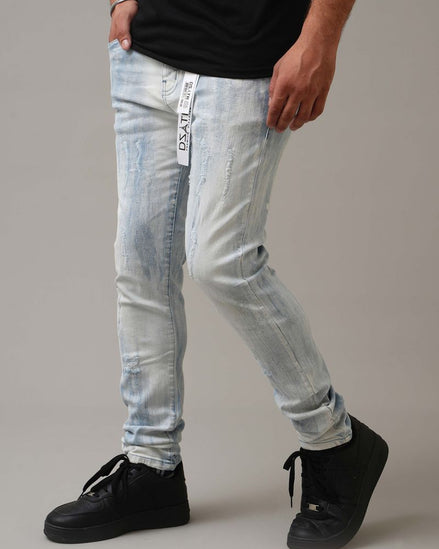 Person wearing light blue distressed jeans with a brand logo and black sneakers on a neutral background