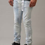 Person wearing light blue distressed jeans with a brand label and black shoes on a gray background