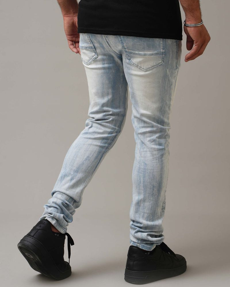 Person wearing light blue jeans and black shoes on a plain background