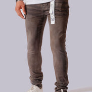 A person wearing slim-fit gray washed jeans with white sneakers, shown from the waist down against a light gray studio background. A white hangtag is visible at the waistband.