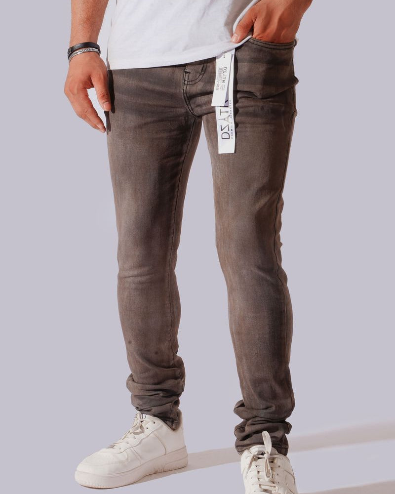 A person wearing slim-fit gray washed jeans with white sneakers, shown from the waist down against a light gray studio background. A white hangtag is visible at the waistband.