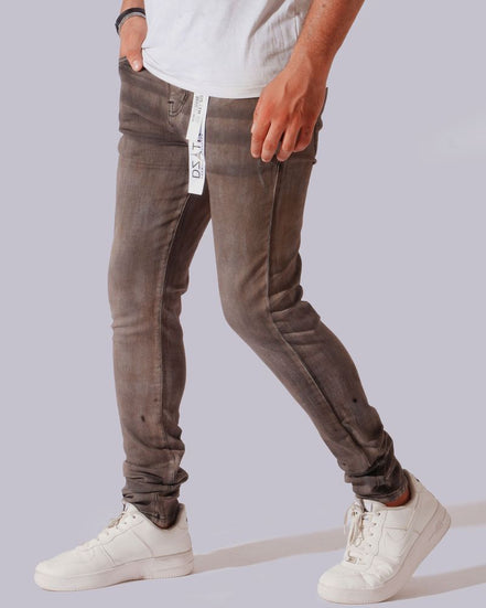 A person wearing slim-fit brown washed jeans with a white t-shirt and white sneakers, shown from the waist down against a light gray background.
