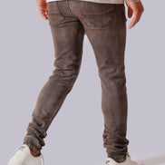 A person shown from the back wearing slim-fit grayish-brown jeans, a white t-shirt, and white sneakers against a light gray studio background.