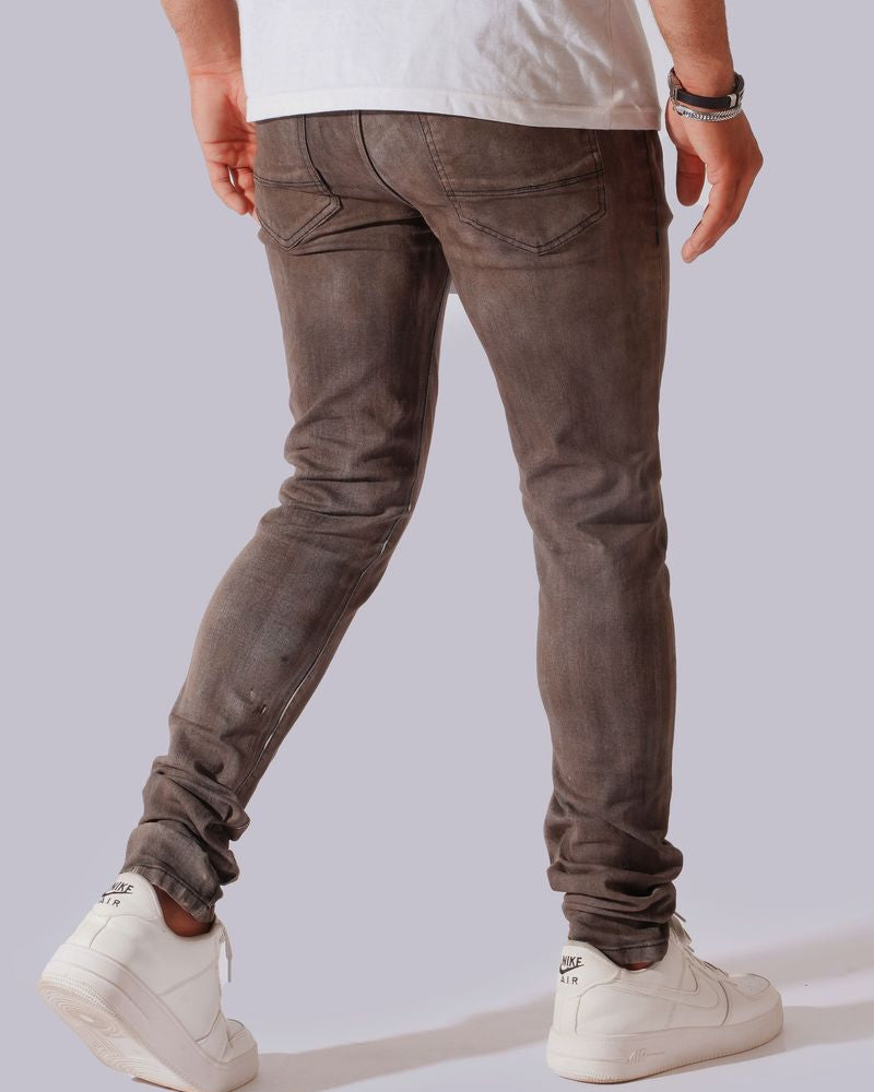 A person shown from the back wearing slim-fit grayish-brown jeans, a white t-shirt, and white sneakers against a light gray studio background.
