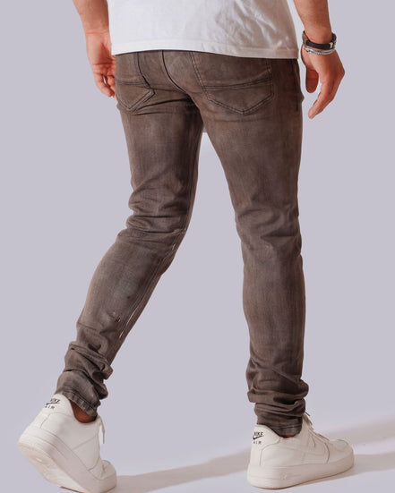 A person shown from the back wearing slim-fit grayish-brown jeans, a white t-shirt, and white sneakers against a light gray studio background.