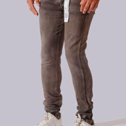 A person wearing slim-fit gray washed jeans with a white waistband tag, paired with a white t-shirt and white sneakers, shown from the waist down against a light gray studio background.