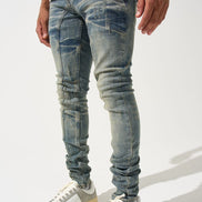Person wearing distressed blue jeans and white sneakers on a light gray background