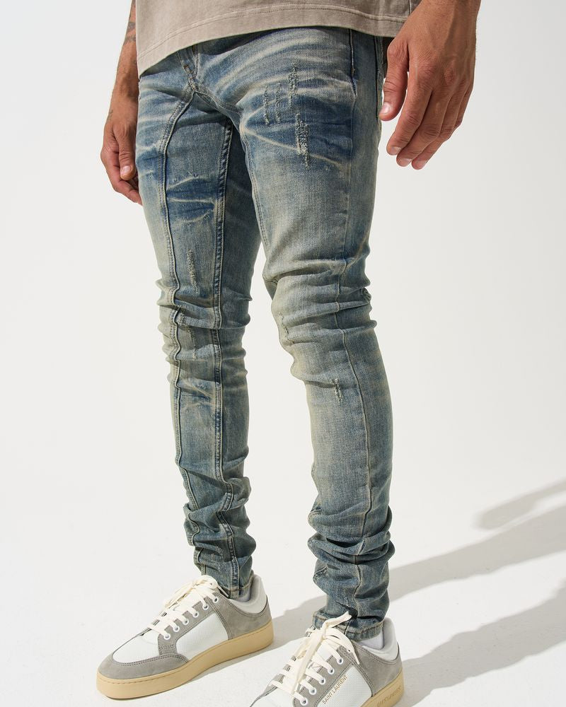 Person wearing distressed blue jeans and white sneakers on a light gray background