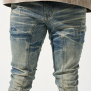 Blue distressed jeans worn with a beige oversized shirt on a white background
