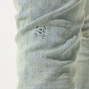 Close-up of light blue denim jeans with a brand logo on the pocket.