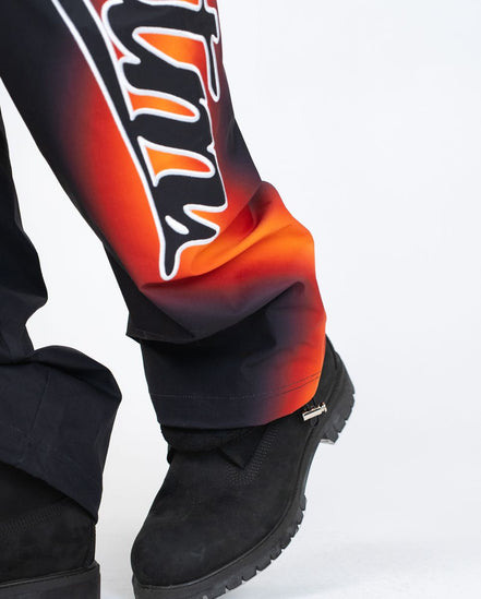 Close-up of a person wearing black boots and colorful pants with flame design on a white background