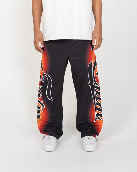 Person wearing black sweatpants with red and orange designs on a white background