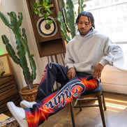 Person sitting on a chair wearing colorful pants with a brand logo, surrounded by plants and a speaker.