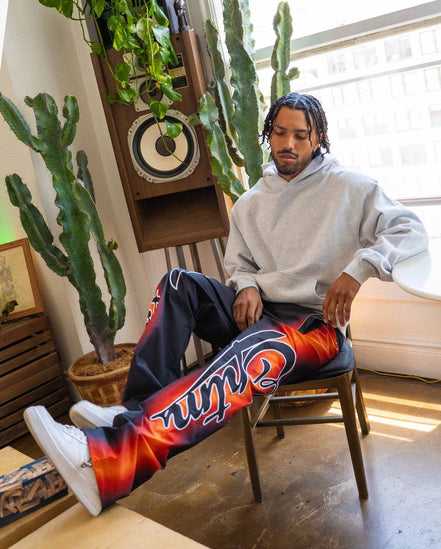 Person sitting on a chair wearing colorful pants with a brand logo, surrounded by plants and a speaker.
