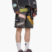 Person wearing a black jacket and gray shorts with various patches on a white background