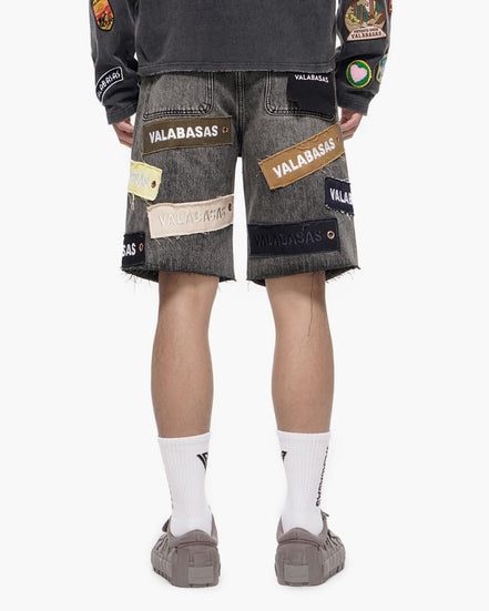Person wearing gray shorts with patches and a dark shirt on a white background