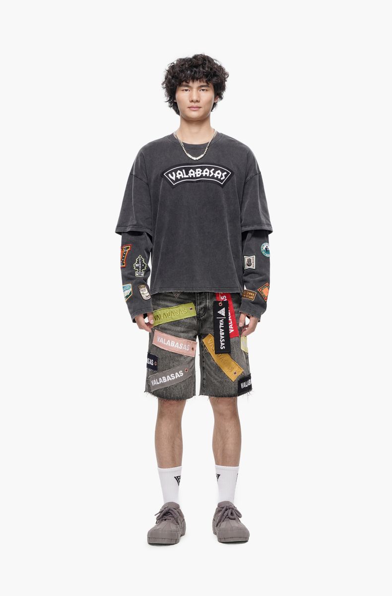 Person wearing a dark gray t-shirt with colorful patches and shorts on a white background