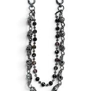 A gothic-style beaded chain accessory featuring antique silver-toned skull charms, faceted dark beads, and silver spacer beads, displayed on a clean white background.