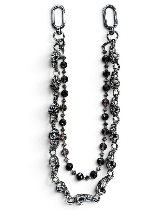 A gothic-style beaded chain accessory featuring antique silver-toned skull charms, faceted dark beads, and silver spacer beads, displayed on a clean white background.