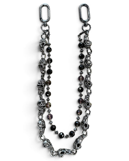 A gothic-style beaded chain accessory featuring antique silver-toned skull charms, faceted dark beads, and silver spacer beads, displayed on a clean white background.