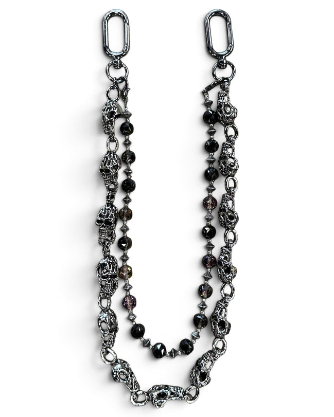 A gothic-style beaded chain accessory featuring antique silver-toned skull charms, faceted dark beads, and silver spacer beads, displayed on a clean white background.