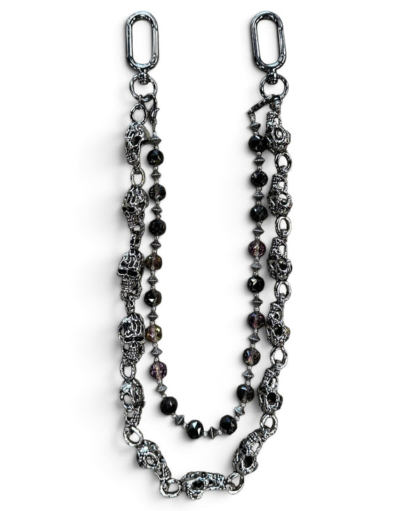 A gothic-style beaded chain accessory featuring antique silver-toned skull charms, faceted dark beads, and silver spacer beads, displayed on a clean white background.