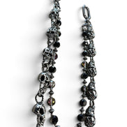 A gothic-style chain accessory featuring antique silver skull charms, faceted black beads, and small metallic spacer beads, displayed on a clean white background.