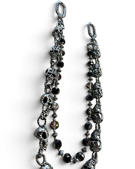 A gothic-style chain accessory featuring antique silver skull charms, faceted black beads, and small metallic spacer beads, displayed on a clean white background.