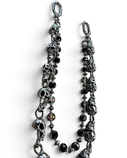 A gothic-style chain accessory featuring antique silver skull charms, faceted black beads, and small metallic spacer beads, displayed on a clean white background.