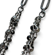 A close-up of a gothic-style metal chain accessory featuring skull charms, faceted black beads, and ornate links, shown against a plain white background.